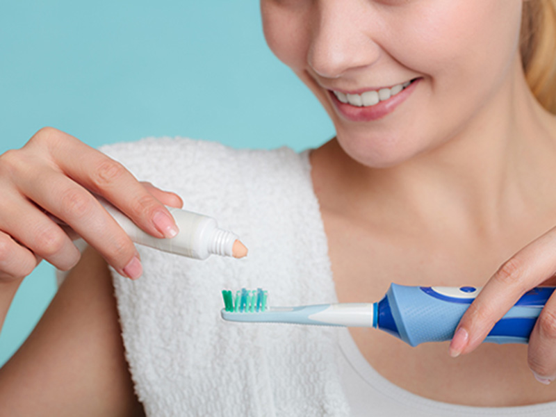 women applying toothpaste on electric toothbrush